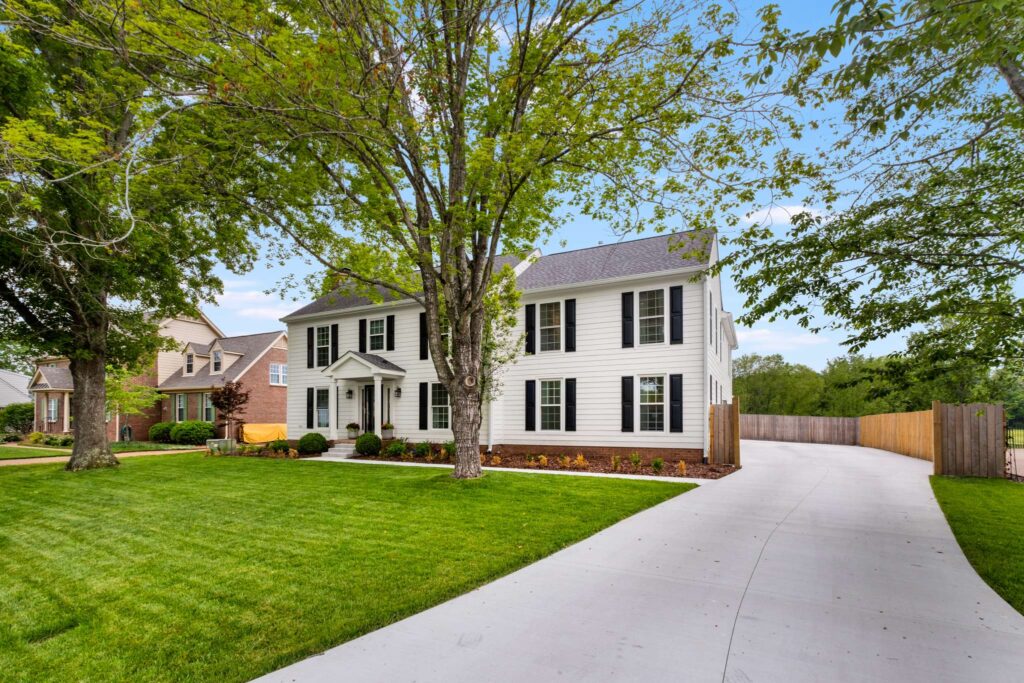 1 A white two-story house with black shutters and front door. A large trees stand in the front yard and there is landscaping. Contact Lotus Building Group as your home renovation contractor in Nashville, TN.