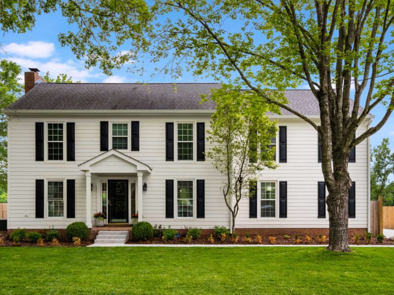 A white two-story house with black shutters and front door. A large trees stand in the front yard and there is landscaping. Contact Lotus Building Group as your home renovation contractor in Nashville, TN.