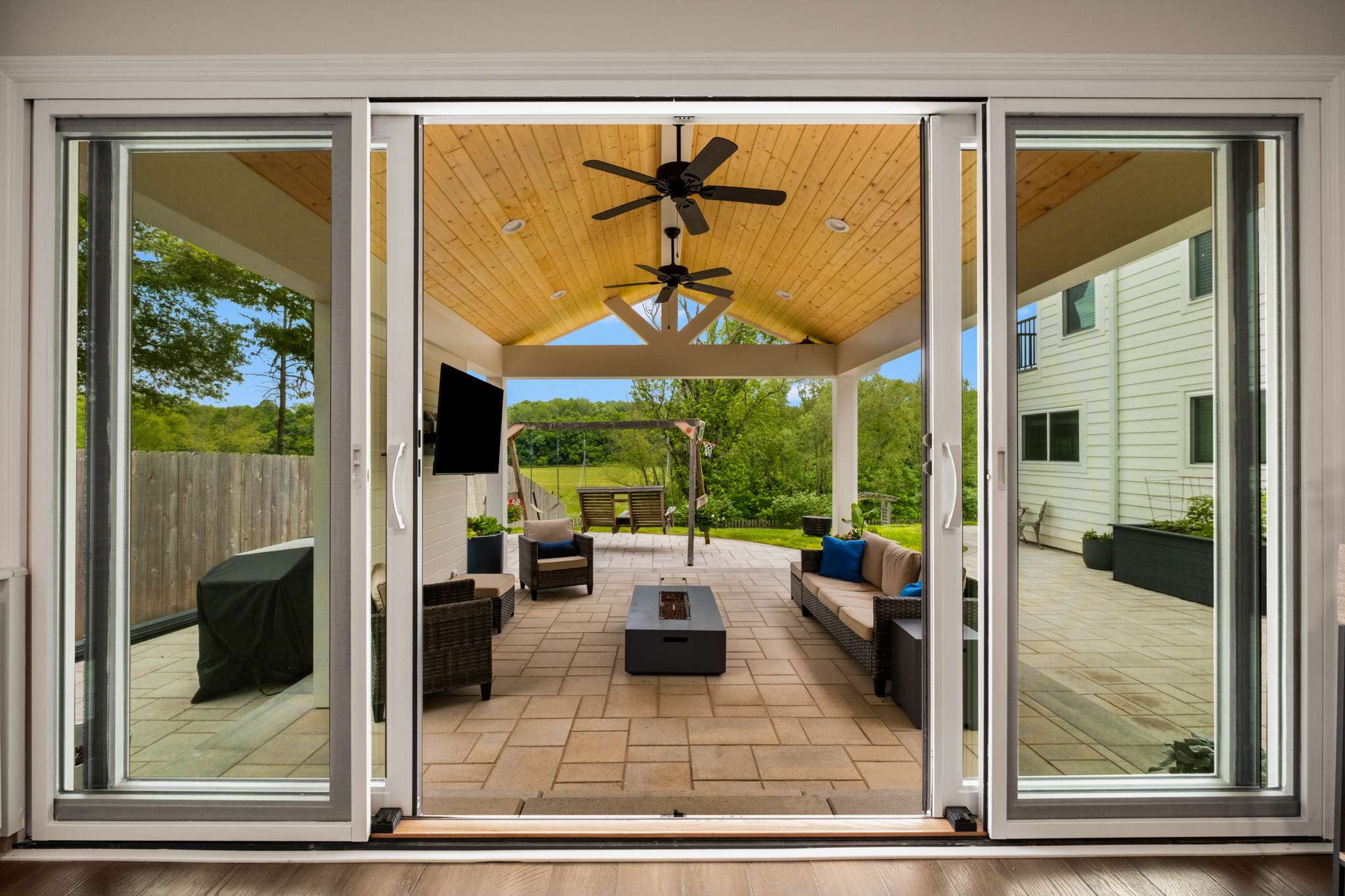 Sliding screen doors open up to a patio with a roof. There's stone and wood accents. There's seating and a flat screen TV. Contact Lotus Building Group for your new home construction projects in Nashville, TN.