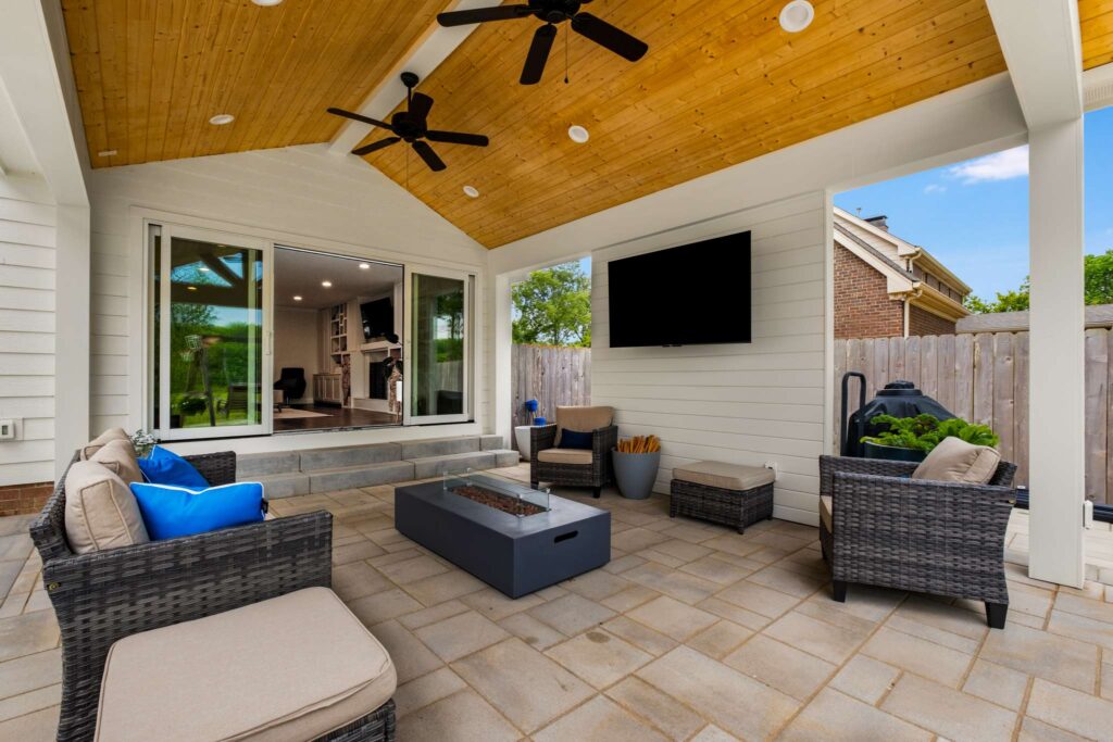 49 Sliding screen doors open up to a patio with a roof. There's stone and wood accents. There's seating and a flat screen TV. Contact Lotus Building Group for your new home construction projects in Nashville, TN.