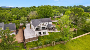 A large two-story white house has a balcony and a patio in the backyard. The patio has a pergola for seating and a swings. Contact Lotus Building Group for your custom home renovations in Nashville, TN.