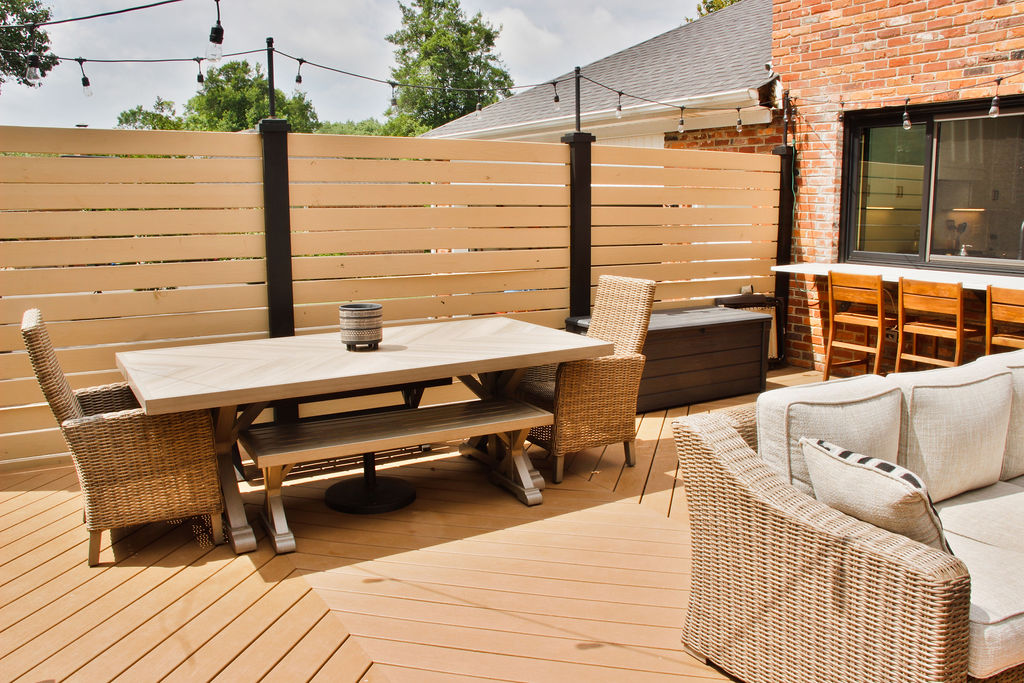 Copy of Deck-Addition-6 On a wooden patio is a long dining table with chairs and benches, bar seating and a couch. Lights hang above the patio. Contact Lotus Building Group as your patio contractor in Nashville, TN.