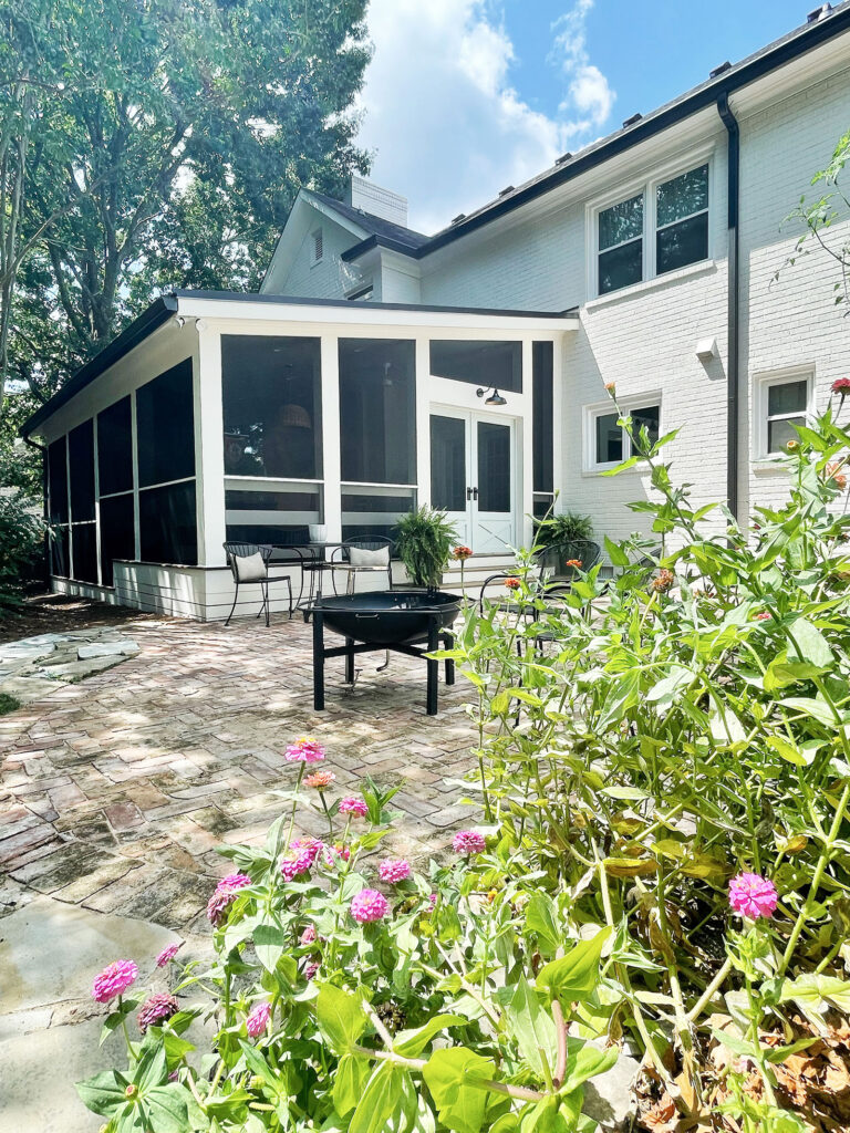 Copy of Screened-In-Porch-1 Lotus Building Group outside house finishes. A white house featuring a sun room that opens up to a brick patio and garden in the backyard. There's seating and a fire pit. Contact Lotus Building Group as your outdoor contractor in Nashville, TN.