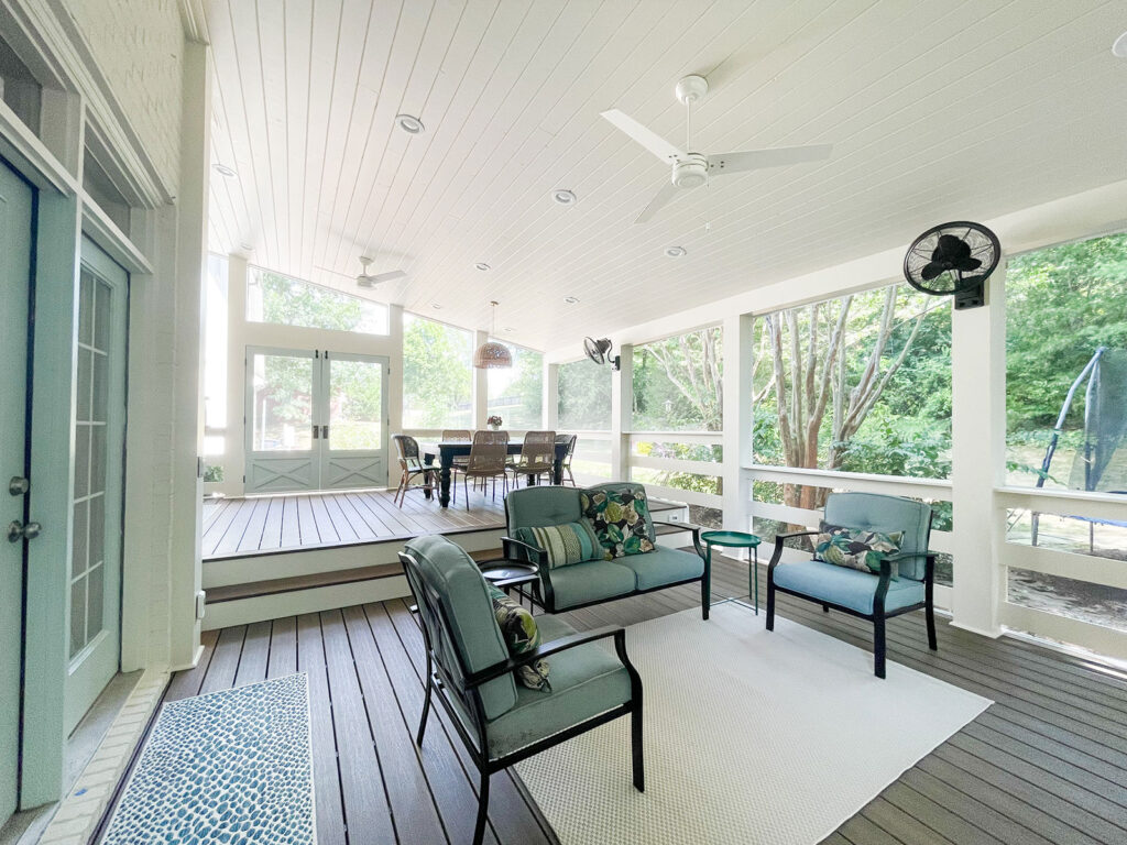Copy of Screened-In-Porch-6 A sunroom has a tall white ceiling with a fan, white wood flooring, and a seating and dining area. The seating and doors are blue. Contact Lotus Building Group as your patio contractor in Nashville, TN.